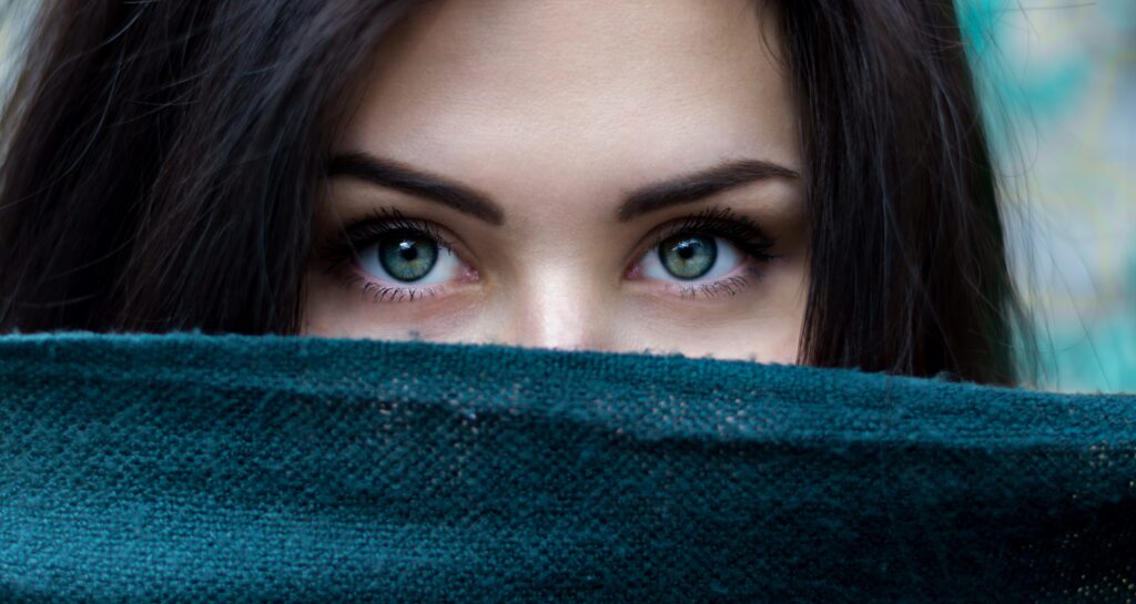 Frau schaut mit ihrem blauen Augen über ein grünes Tuch hinweg